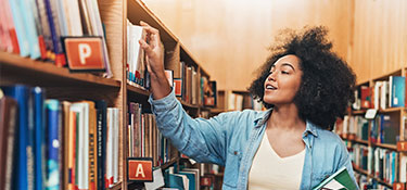 Una mujer mirando sacando un libro del estante mientras está en la biblioteca